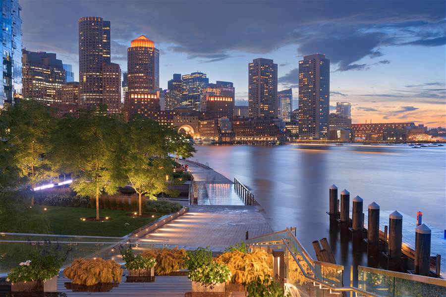 Boston Harborwalk with the downtown skyline lit up at dusk