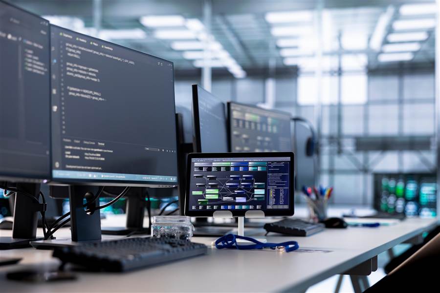 Multiple monitors displaying deployment dashboards and code in an IT office