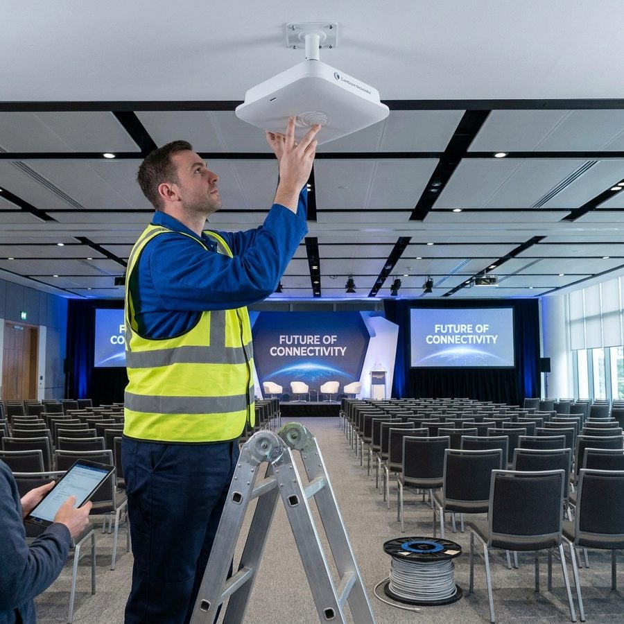 Technician installing a Cambium wireless access point above a conference room